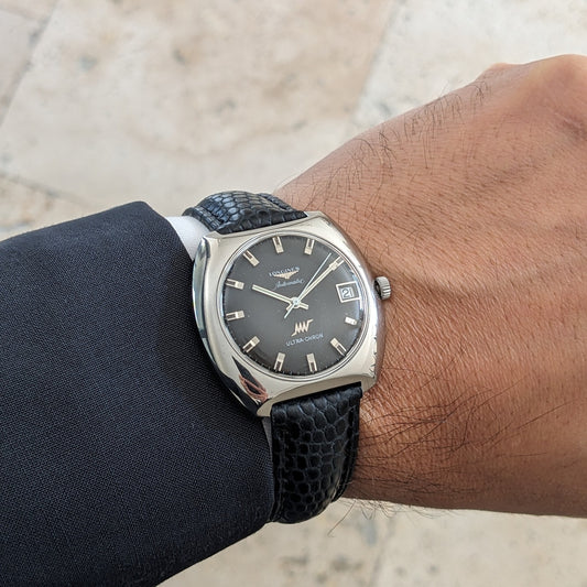 Longines Ultrachron reference 8429 worn on a wrist, showing its dark dial, date window, silver-toned case and black textured strap.