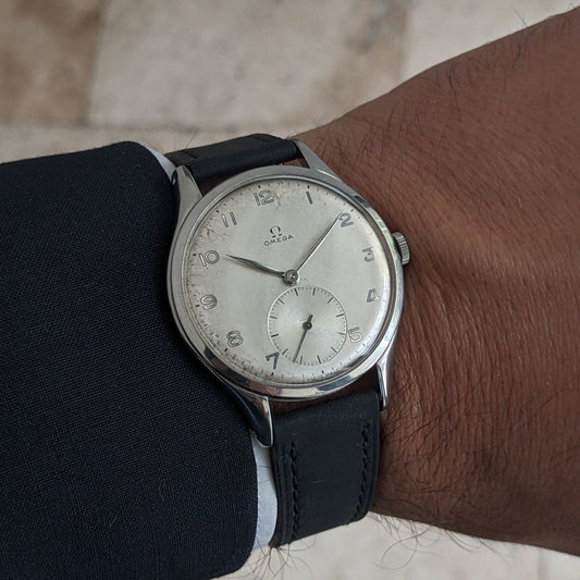 Omega Jumbo reference 2505-5 worn on a wrist beneath a dark sleeve, showing its silver-toned dial and black leather strap.