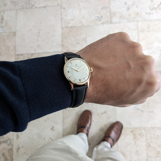 Omega Classic Referenz 14392-61-SC am Handgelenk über einem gefliesten Boden, mit sichtbarem schwarzen Armband und cremefarbenem Zifferblatt.