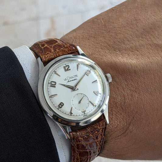 Wrist view of the Jaeger-LeCoultre Automatic E328 with a light dial and brown textured strap against a pale stone background.