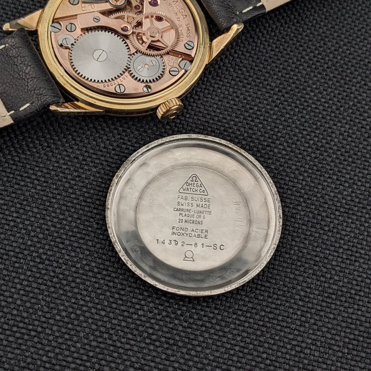 Omega Classic référence 14392-61-SC ouverte, avec le mouvement doré au-dessus et le fond de boîtier intérieur gravé en dessous sur tissu noir.