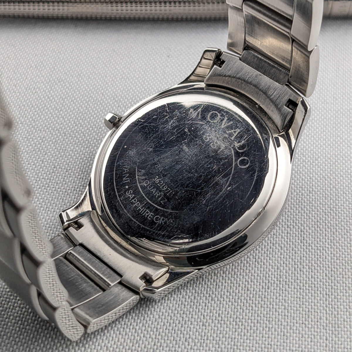 Vue arrière d'une montre Movado avec fond de boîtier circulaire poli, lettrage gravé et maillons de bracelet en acier inoxydable.