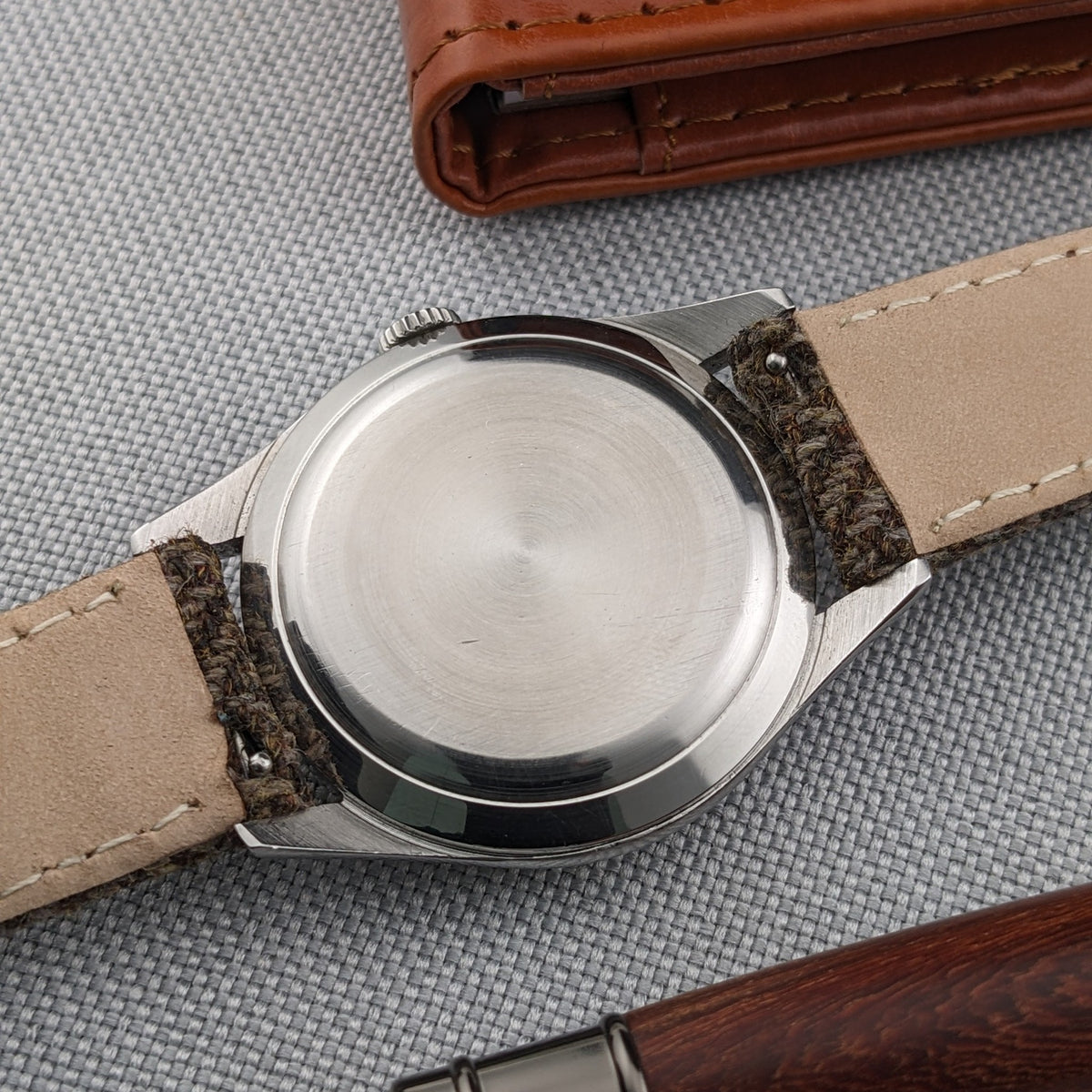 Longines Classic reference 8135-5 shown from the brushed case-back side on a brown woven strap, with a leather wallet and pen nearby.