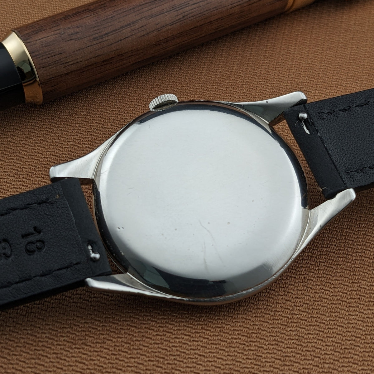 Omega Jumbo reference 2505-5 shown from the rear with a plain reflective caseback, black leather strap, and wooden pen on brown fabric.
