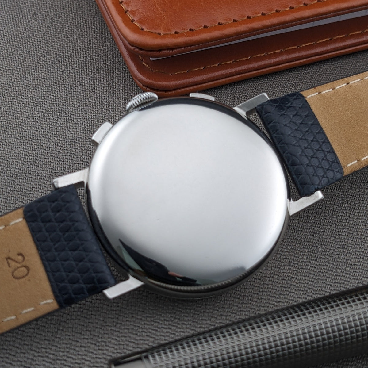 Eberhard & Co.. Pre-Extra Fort shown from the back with a polished round case, blue strap, brown wallet and pen on textured fabric.