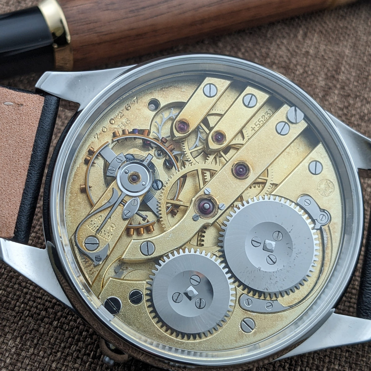 IWC Schaffhausen कलाई घड़ी का पारदर्शी केस बैक के माध्यम से दिखाया गया, गिल्ट मूवमेंट के साथ पुल, गियर्स और स्क्रूज़ को प्रकट करता हुआ।