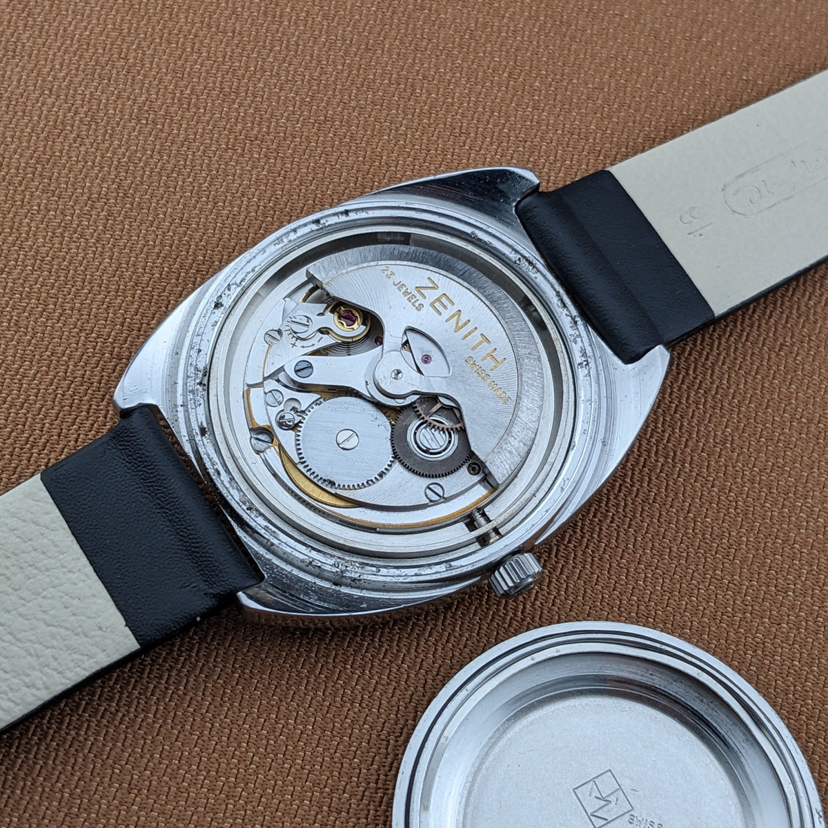 Open-back Zenith Automatic reference GR 720001 showing the mechanical movement, black strap, and separate circular caseback on brown fabric.