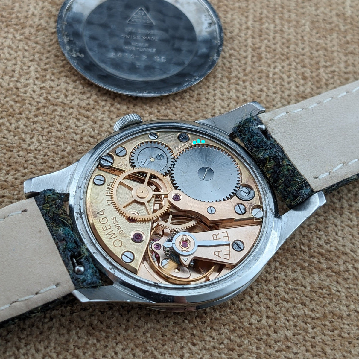 Omega Classic Referenz 2810-2 SC geöffnet auf gewebtem Stoff, mit sichtbarem mechanischem Uhrwerk, Zahnrädern, Brücken und gefassten Komponenten.