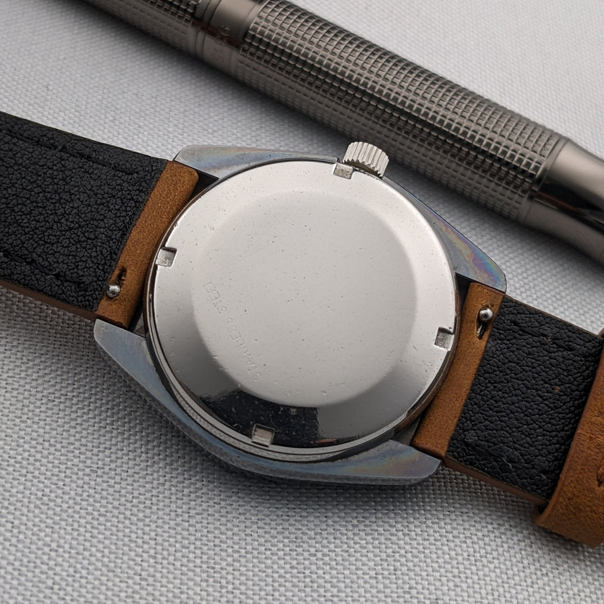 Rear view of the LONGINES Automatic reference 3042-633 with a round closed caseback, brown leather strap and textured metal pen.