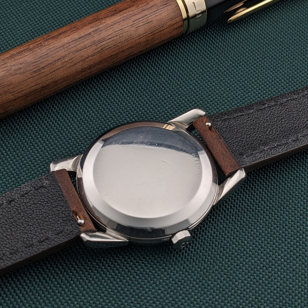 Omega Automatic Bumper reference 2767-4 SC shown from the rear on a brown leather strap, with a polished circular caseback centered on textured green fabric.