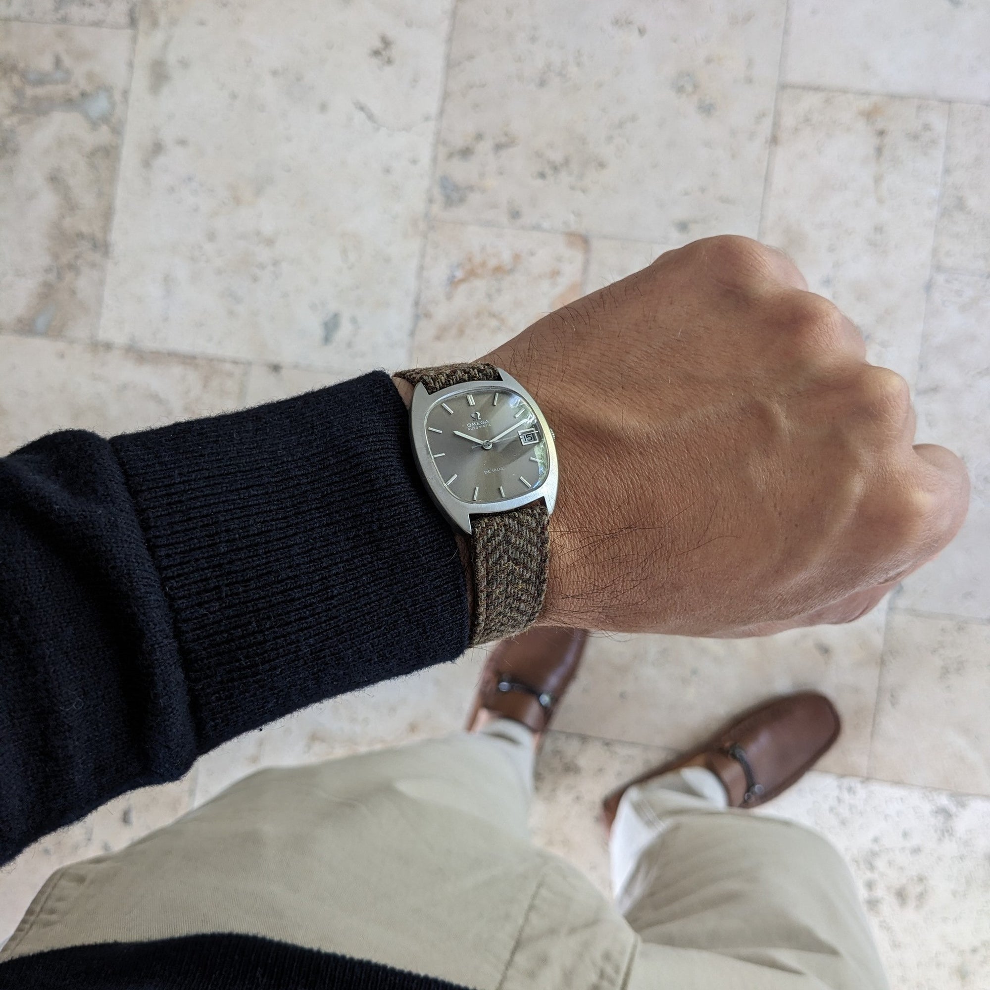 Omega Dr Ville Automatic ref. 162.045 worn on a wrist, showing its silver cushion-shaped dial and brown woven strap over tiled flooring.