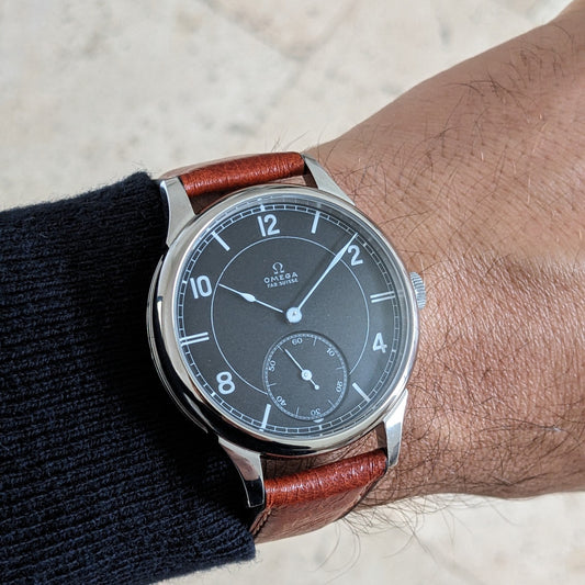 Omega wristwatch with dark dial, Arabic numerals, small seconds subdial, polished case, and brown leather strap shown on a wrist.