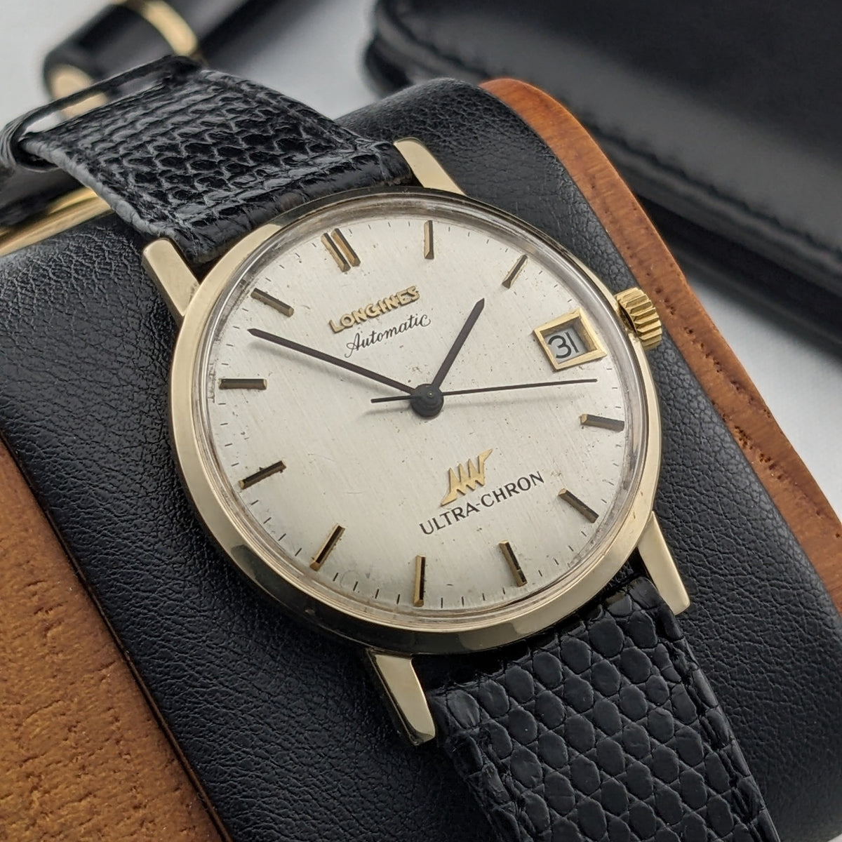 Close view of the Longines Ultra-Chron 69-556AC dial showing gold-tone indices, hands, date window, and black textured strap over leather.