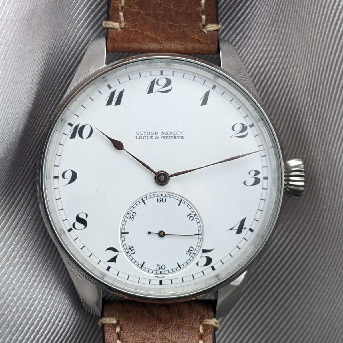 Ulysse Nardin Locle & Genève कलाई घड़ी सफेद डायल, काले अरबी अंक, केंद्रीय हाथ और छोटे सेकंड सबडायल के साथ।