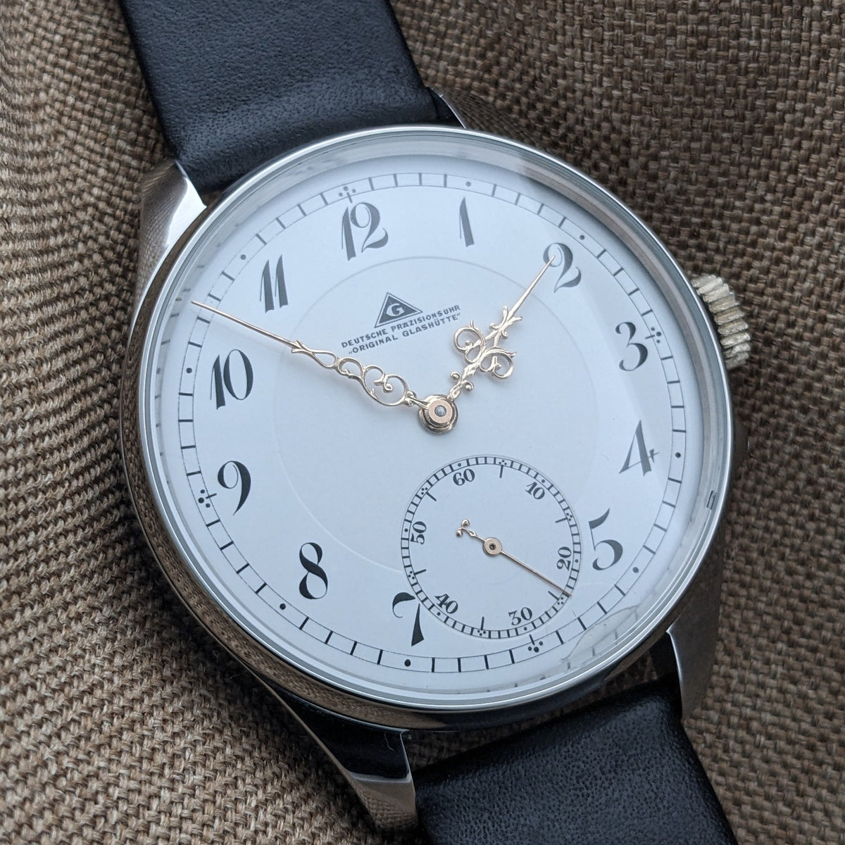 Deutsche Präzisionsuhr „Original Glashütte” mit weißem Zifferblatt, stilisierten schwarzen arabischen Ziffern, verzierten goldfarbenen Zeigern