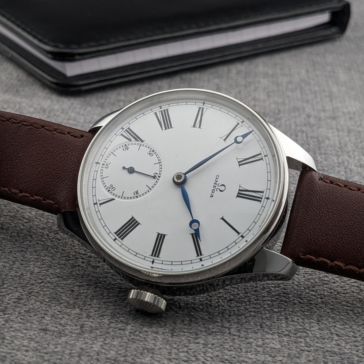 Orologio Omega con quadrante bianco a numeri romani, lancette blu, sub-quadrante dei secondi, cassa lucida e cinturino in pelle marrone.
