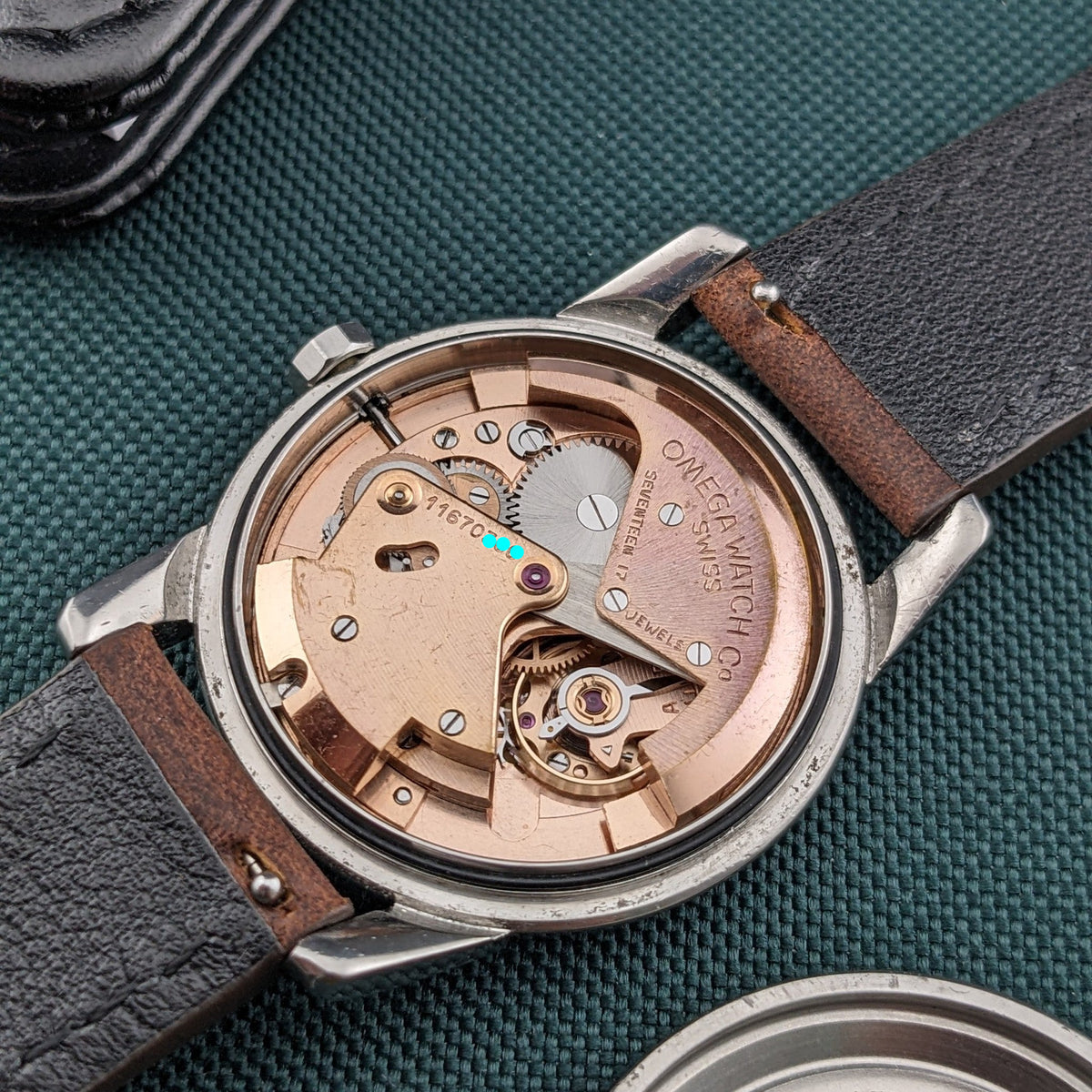 Open Omega Automatic Bumper reference 2767-4 SC displaying its copper-toned mechanical movement, rotor, screws and balance assembly on green fabric.