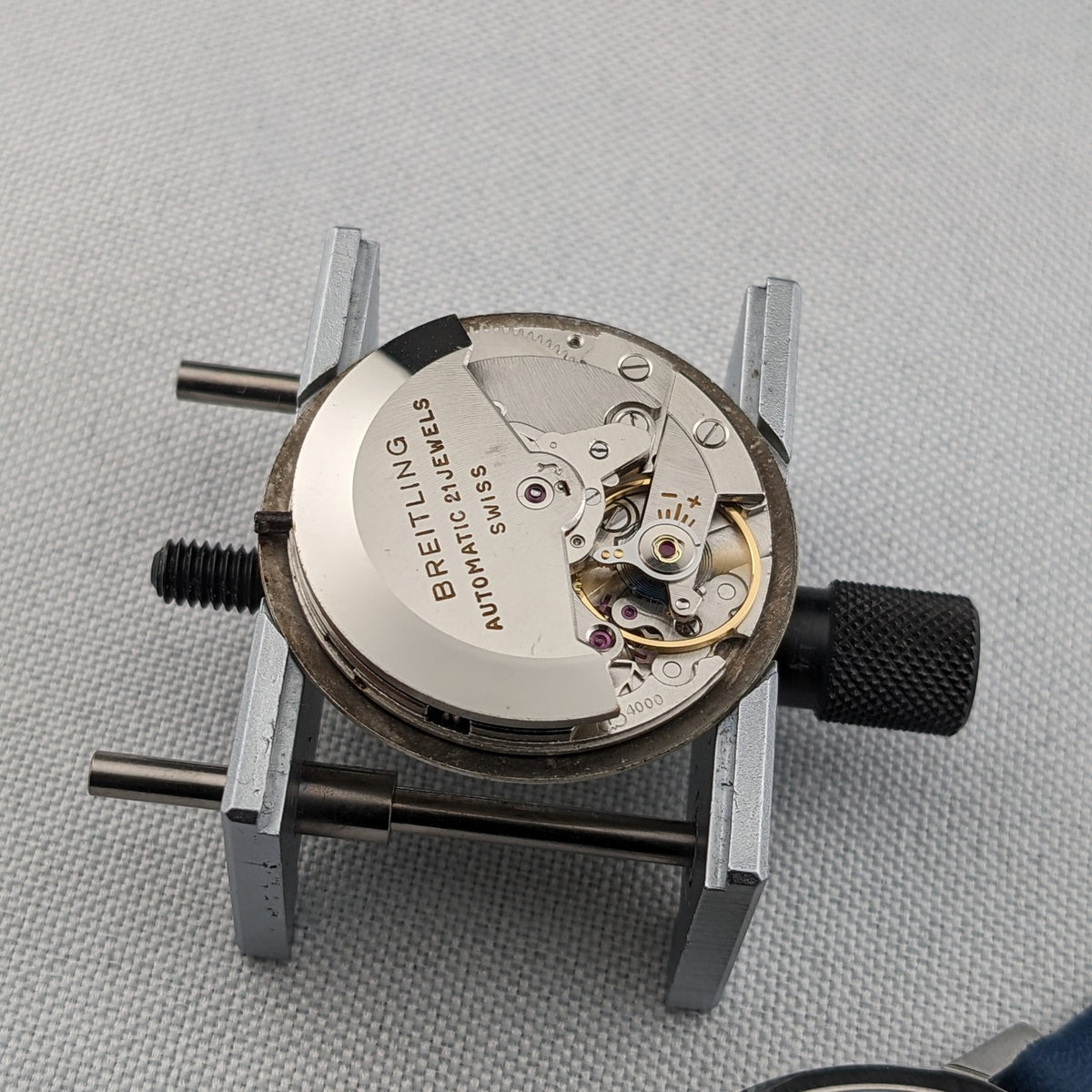 Breitling Automatic watch movement displayed in a metal holder, with the rotor, gears and balance assembly visible.