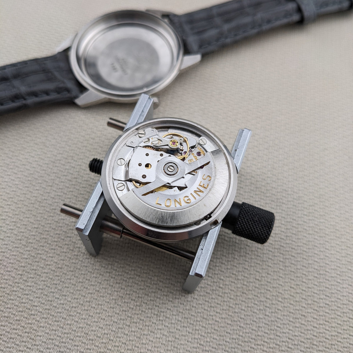 Longines Ultra-Chron 7827 movement displayed outside the case, with the exposed Longines mechanism in the foreground and case behind.
