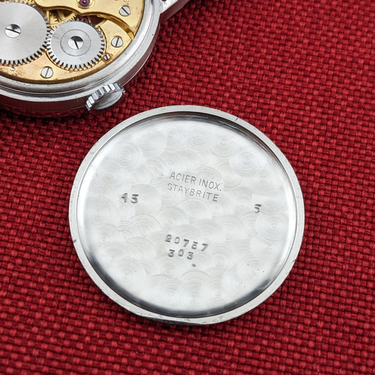 Longines Calatrava reference 20757 caseback interior displayed on red fabric, with engraved text and the edge of the watch movement at upper left.