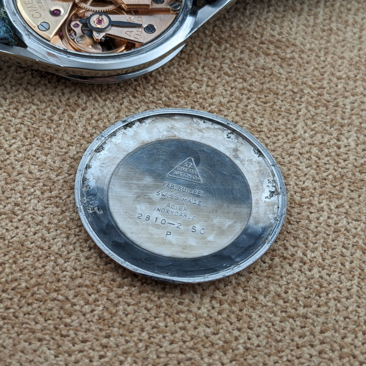Abgenommener Gehäuseboden der Omega Classic Referenz 2810-2 SC auf gewebtem Stoff, mit sichtbaren Gravuren.