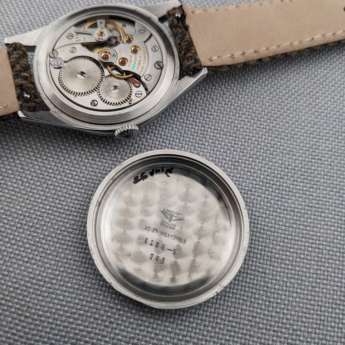 Opened Longines Classic reference 8135-5 displays its mechanical movement above the detached case back, both arranged on gray fabric.
