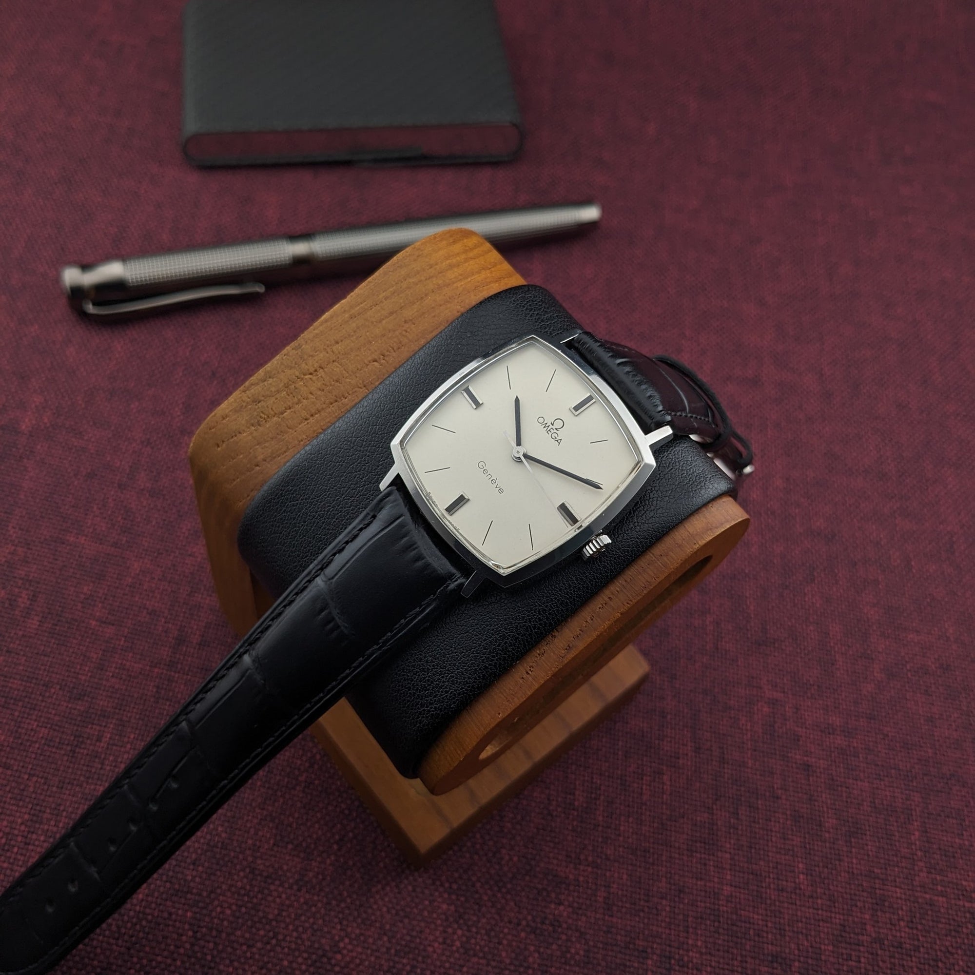 Omega Genève reference 131.022 resting on a wooden stand, showing its cream dial, silver case, and black leather strap.