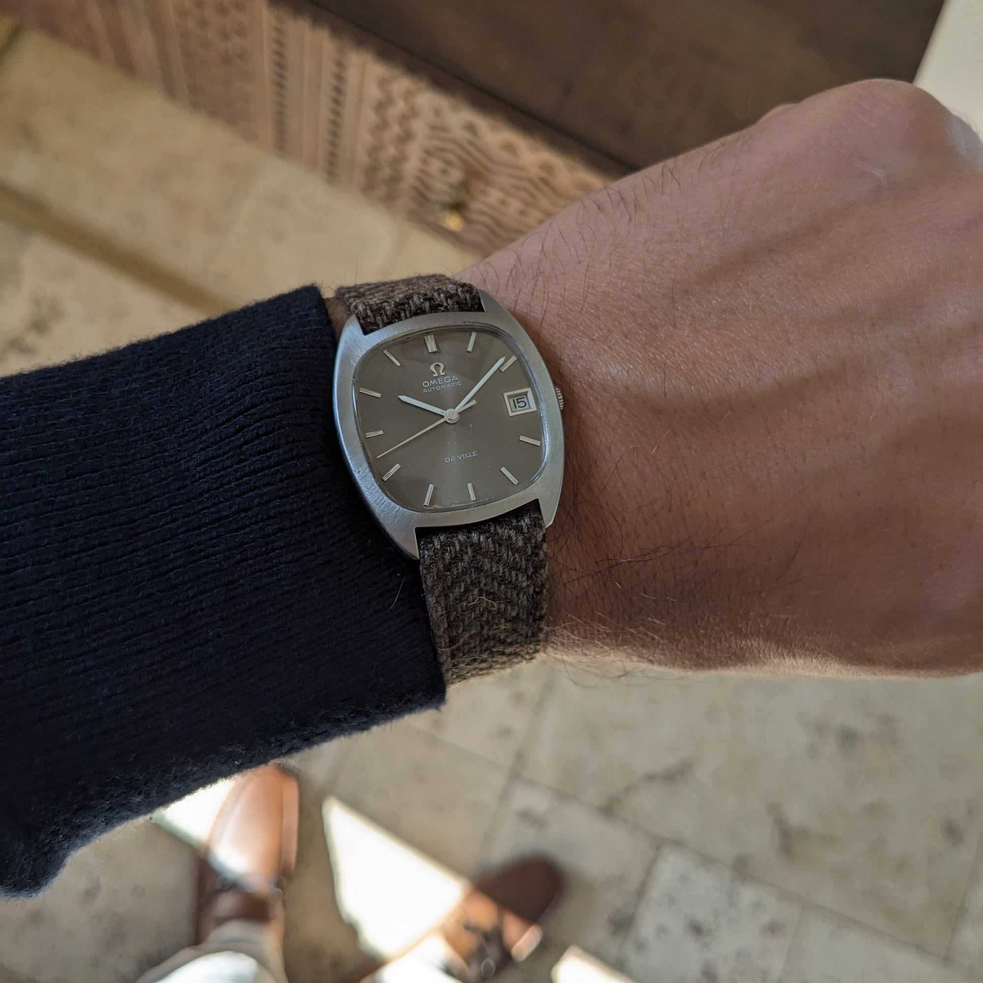 Close wrist view of the Omega Dr Ville Automatic ref. 162.045, with silver dial, date window, and textured brown strap.