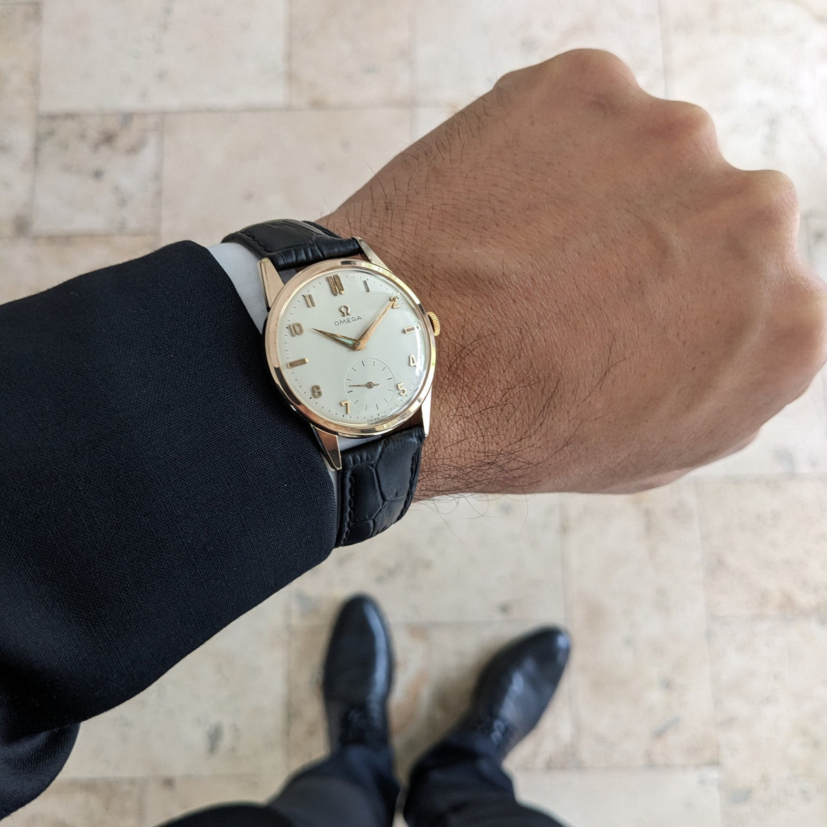 Omega Classic reference 14391-1 viewed on a suited wrist, with the light dial and black strap framed against a tiled floor.