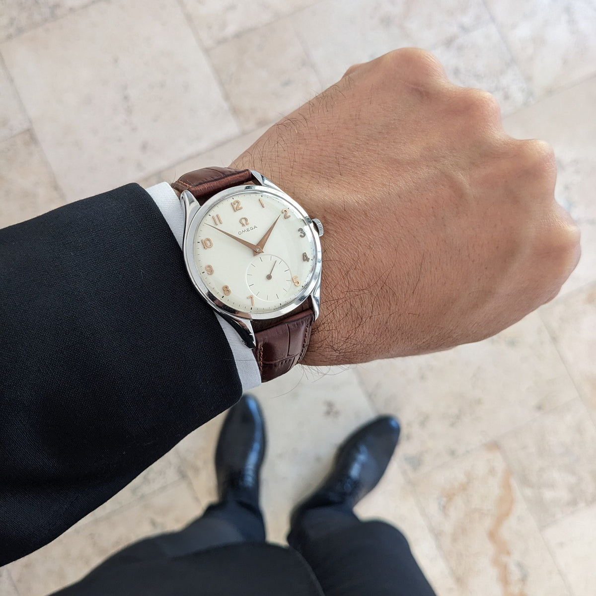 Omega Jumbo Referenz 2505-10 an einem Anzugärmel von oben, mit sichtbarem braunem Armband und hellem Zifferblatt.