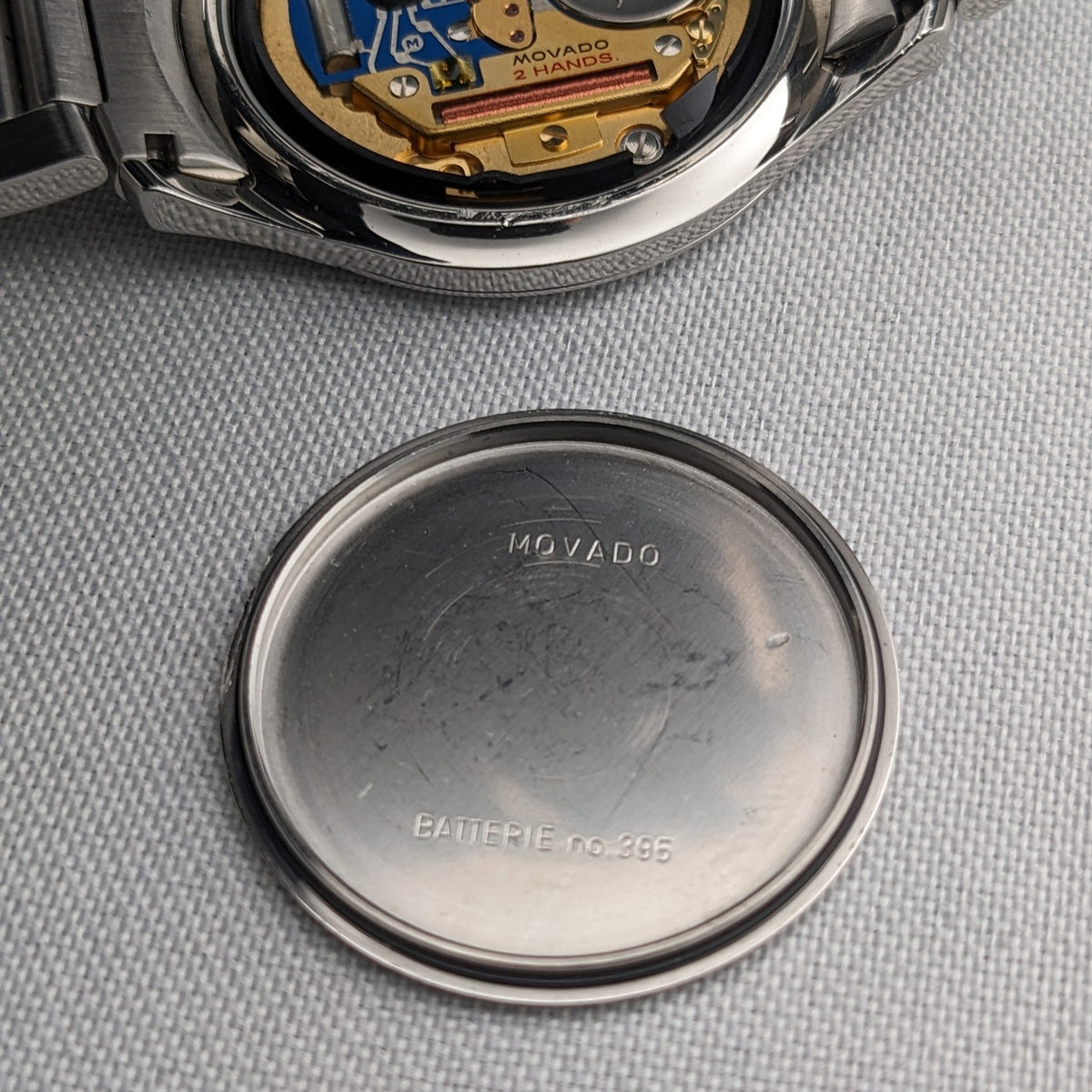 Fond de boîtier Movado détaché affiché sous la montre ouverte, avec lettrage Movado gravé et texte supplémentaire à l'intérieur.