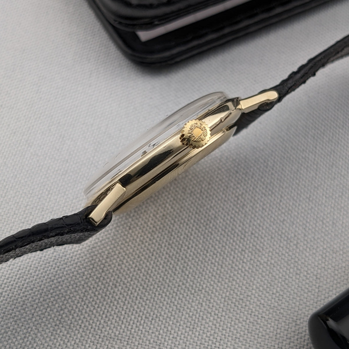 Side profile of the Longines Ultra-Chron reference 69-556AC showing the gold-tone case, ridged crown, crystal edge, lugs, and black strap.