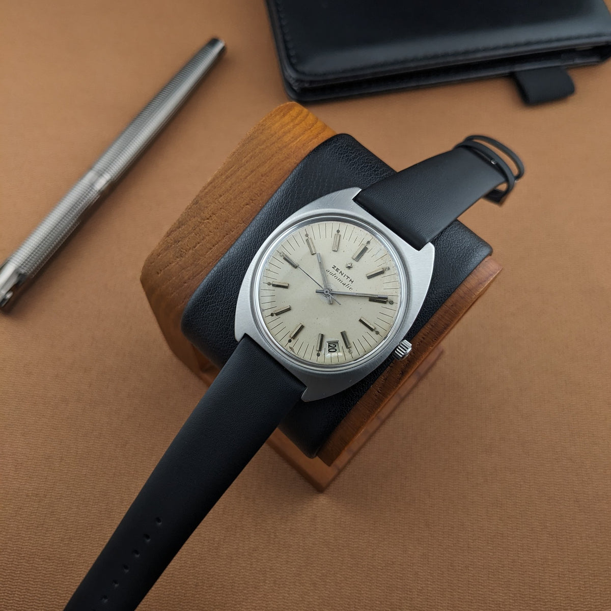 Zenith Automatic reference GR 720001 on a black strap, resting on a wooden watch stand beside a pen and black case.