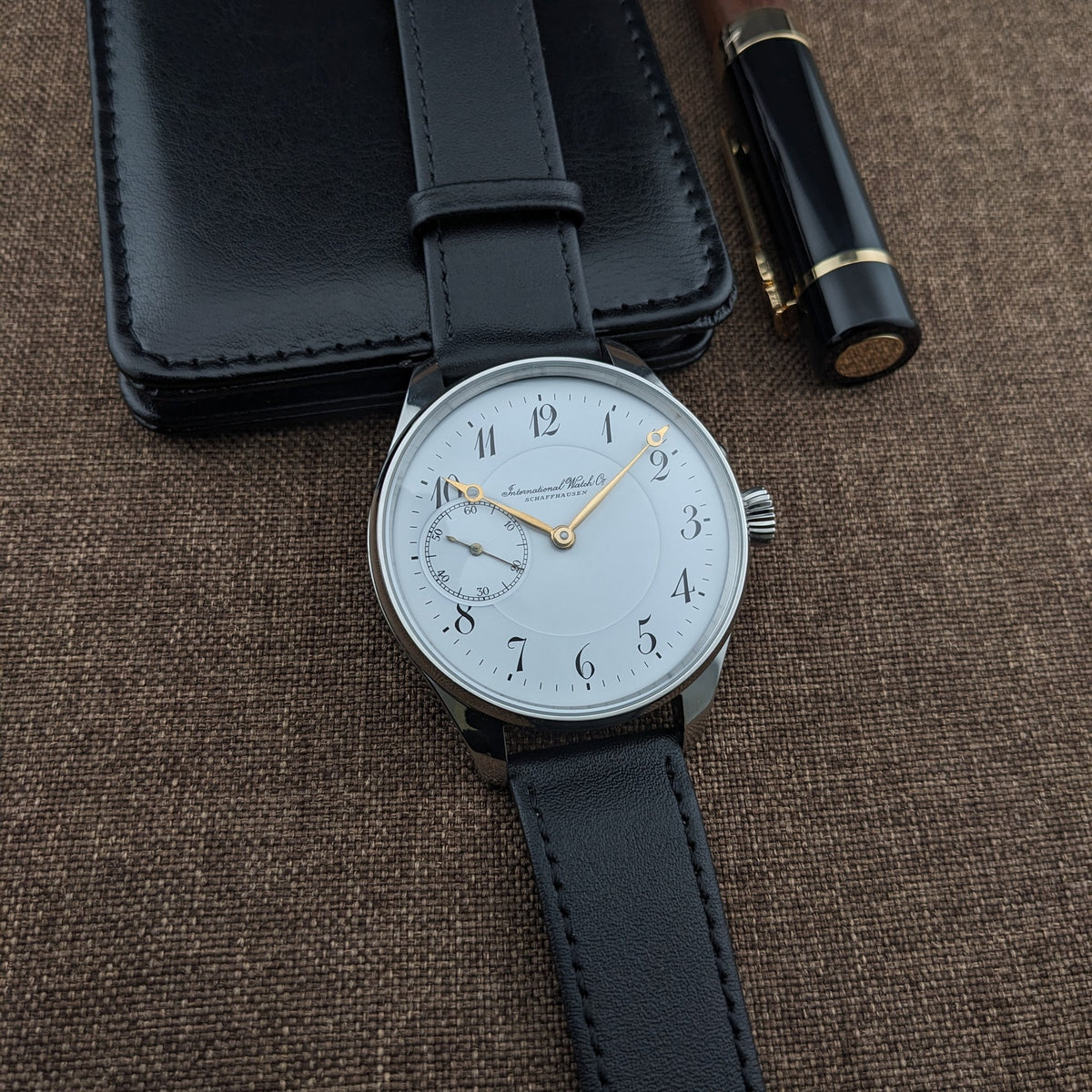 IWC Schaffhausen कलाई घड़ी सफेद डायल, काले अरबी अंक, सुनहरे हाथ, सेकंड्स सबडायल और काले चमड़े की पट्टी के साथ।
