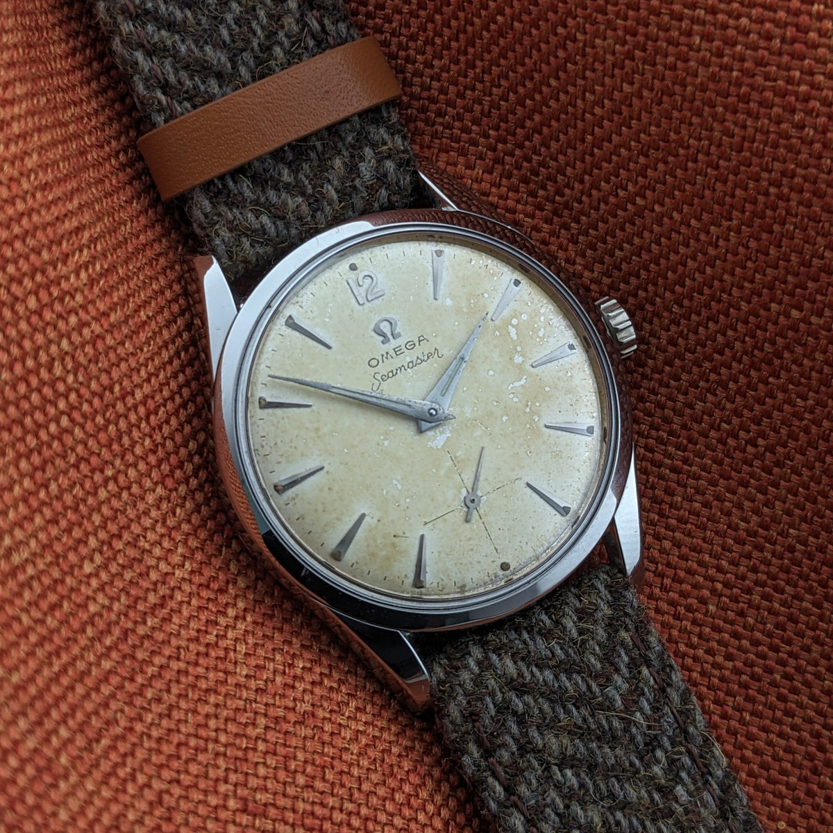 Omega Seamaster reference 29374 at an angle, showing its cream dial, applied hour markers, central hands, seconds subdial and woven strap.