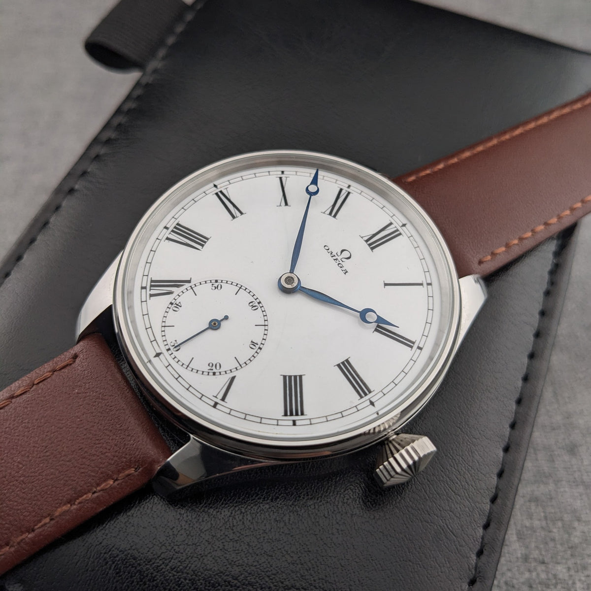 Vista angolata di un orologio Omega con quadrante bianco a numeri romani, lancette blu, registro dei secondi, lunetta argentata e cinturino marrone.