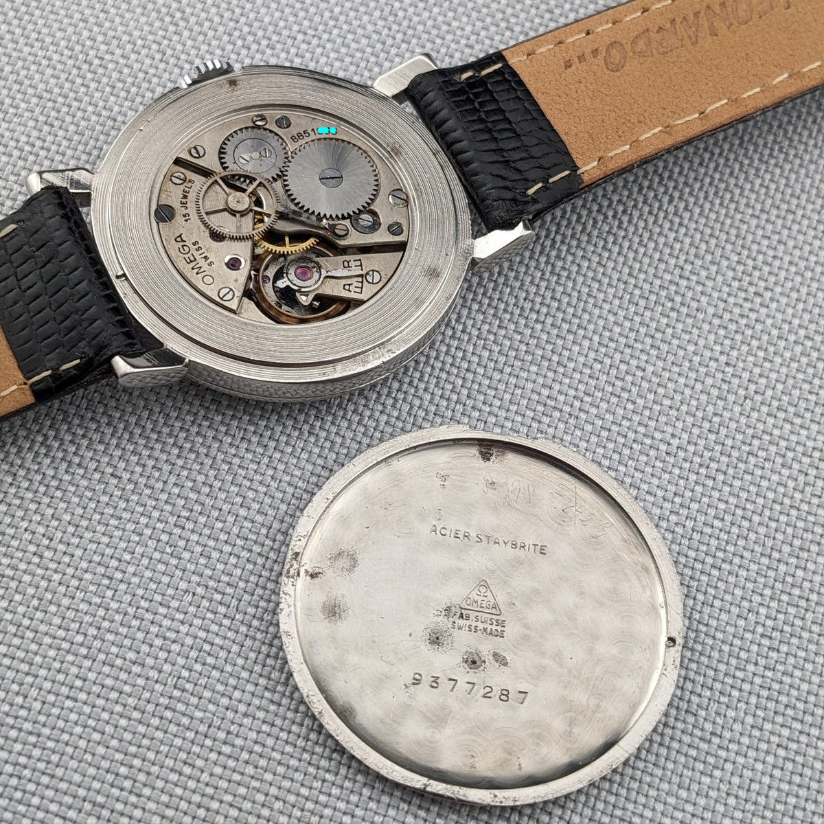 Omega movement and detached caseback displayed together; the back shows engraved markings and the number 9377287.
