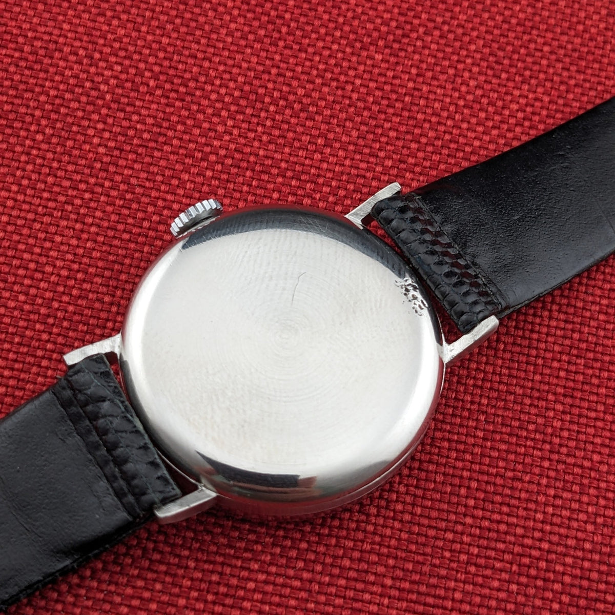 Rear view of the Longines Calatrava reference 20757 on a black strap, showing its smooth round caseback against red fabric.