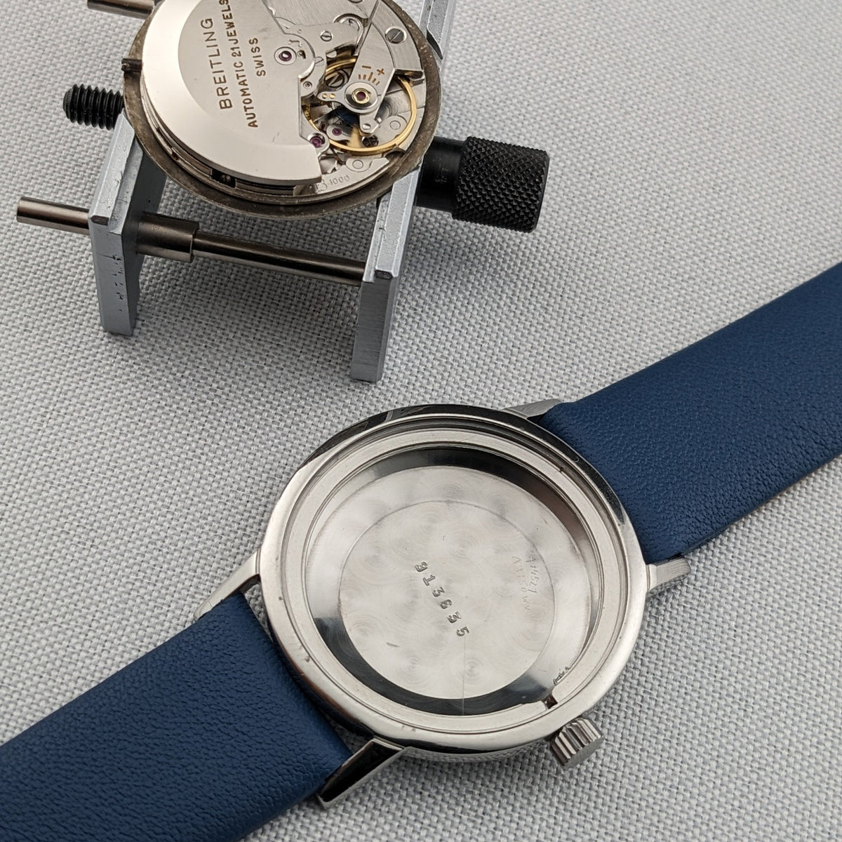 Breitling Automatic watch caseback rests beside its exposed movement, showing the blue strap and circular inner case.