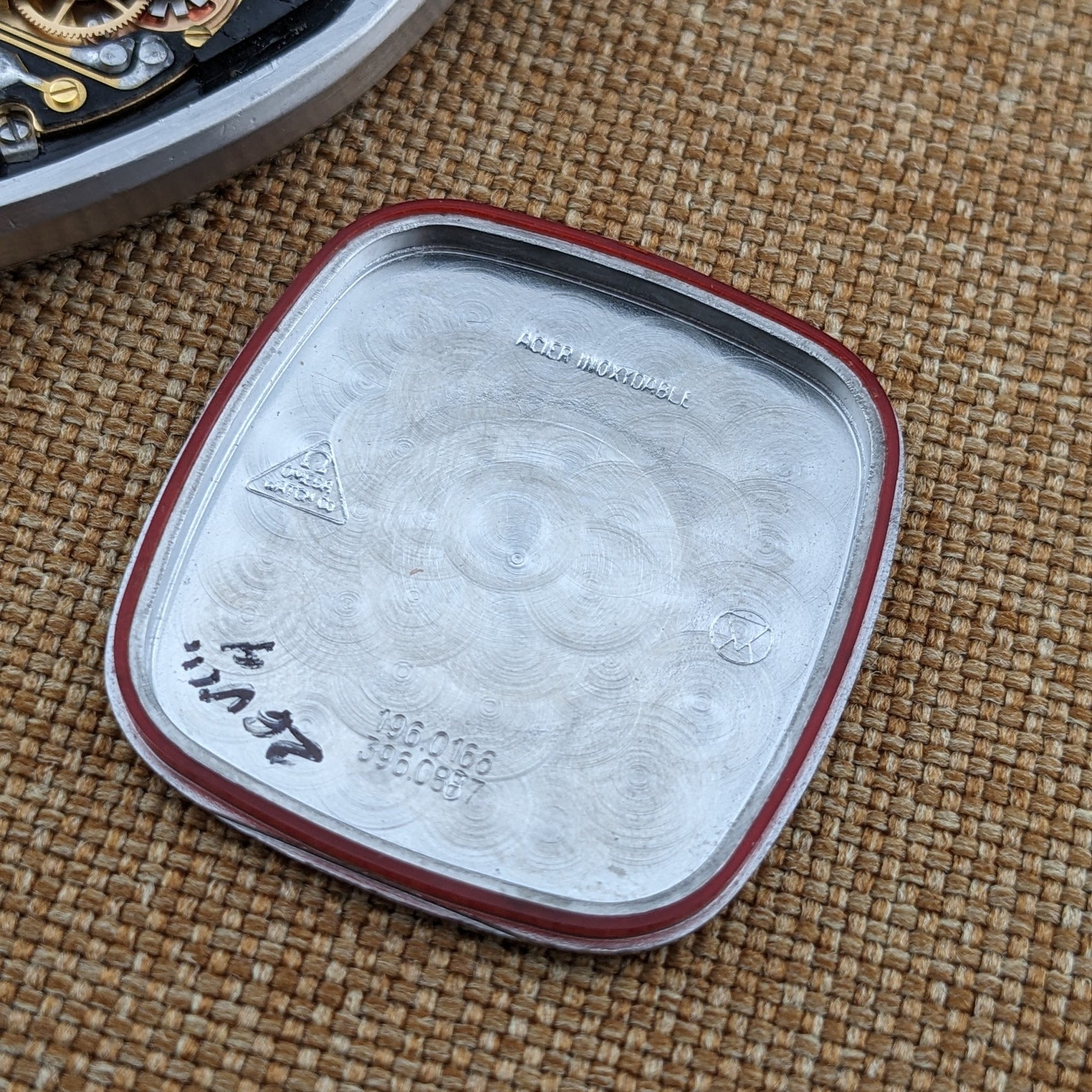 Interior of the Omega Seamaster reference 196.0166 caseback shown separately, with engraved markings and a red gasket around the rim.