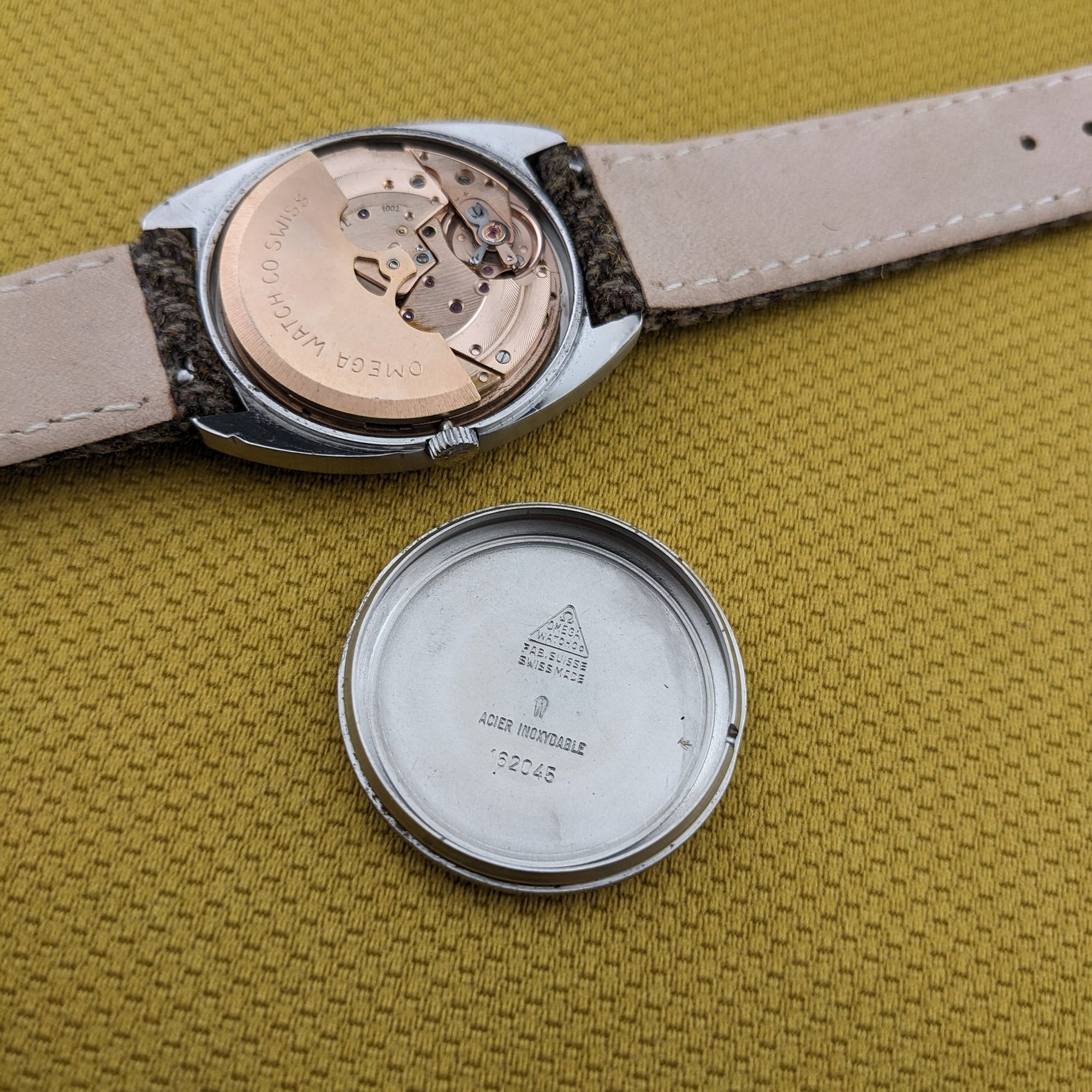 Omega Dr Ville Automatic ref. 162.045 shown open on yellow fabric, with the movement exposed and the separate inner caseback beside it.