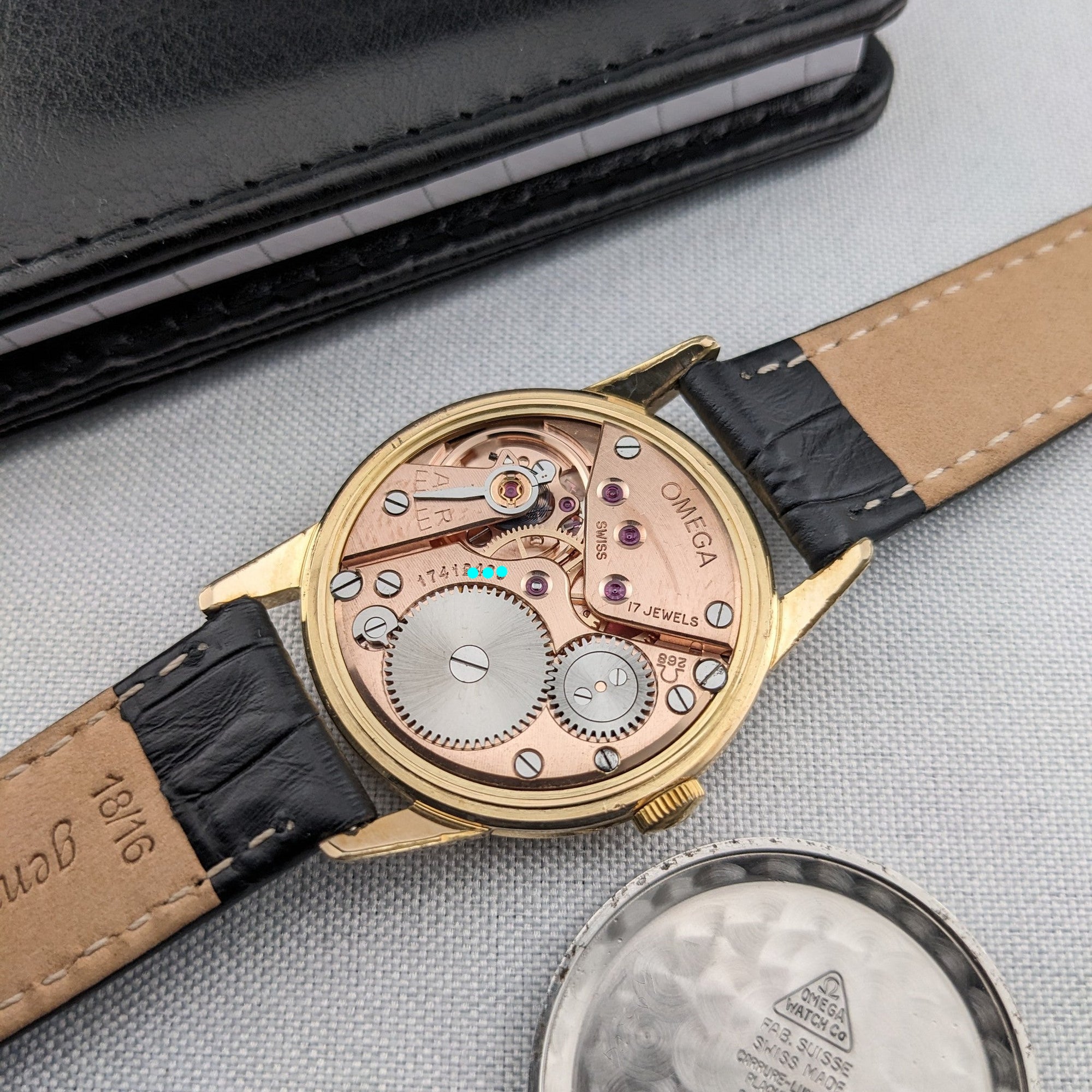 Reverse view of the Omega Classic reference 14391-1, showing the mechanical movement, black strap and detached caseback on fabric.