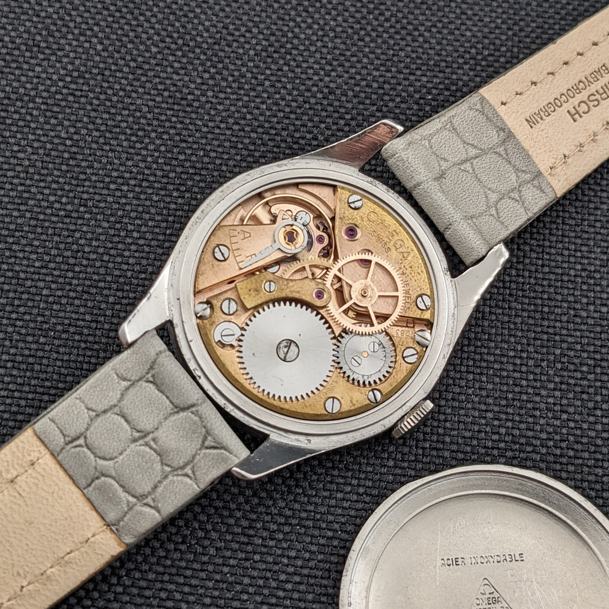 Omega Classic Referenz 2760-6 SC von hinten geöffnet, zeigt das mechanische Werk, graues Armband und separaten runden Gehäuseboden.