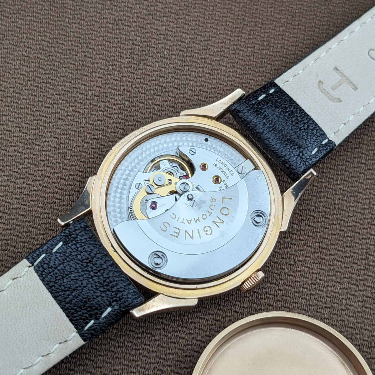 Offener Gehäuseboden der Longines Automatik Referenz 6058, zeigt das Uhrwerk, den Rotor, das goldfarbene Gehäuse und das schwarze Lederarmband.