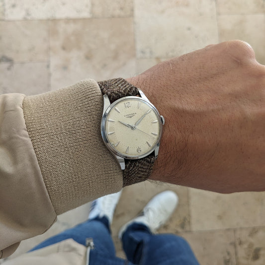 Longines Classic reference 8135-5 worn on a wrist, showing its light dial, brown woven strap and silver case against an outdoor background.