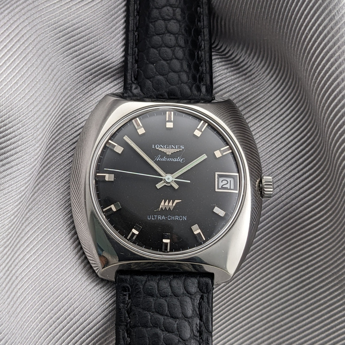 Front view of the Longines Ultrachron reference 8429 with dark dial, baton markers, date window, black strap and silver-toned case.