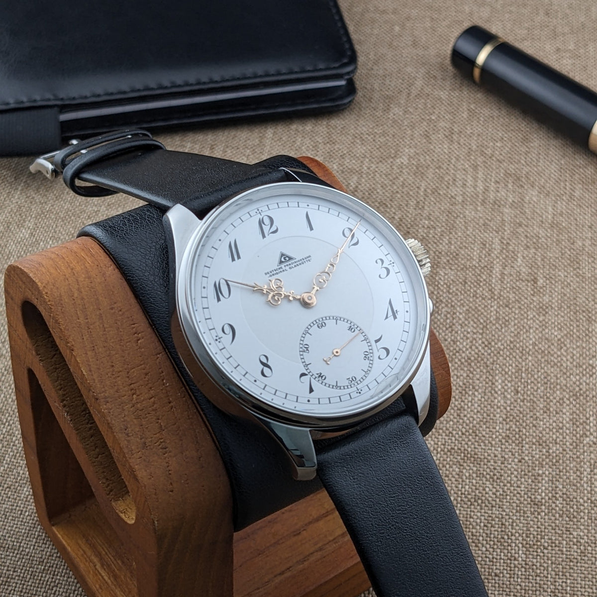 Deutsche Präzisionsuhr „Original Glashütte” auf einem Holzständer, zeigt das weiße Zifferblatt, schwarzes Armband und pol