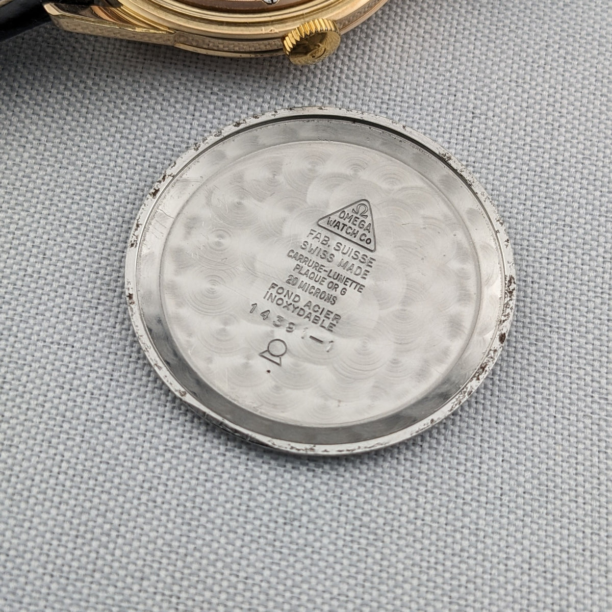 Interior of the Omega Classic reference 14391-1 caseback, with visible Omega markings and engraved text on the patterned metal surface.