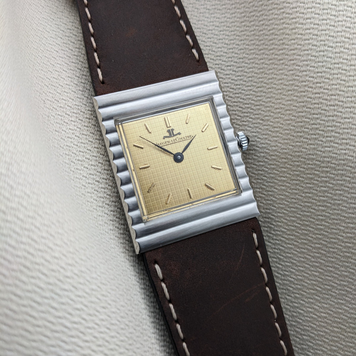 Schrägansicht der Jaeger-LeCoultre Vogue Tank Ref. 9120, hebt das rechteckige Zifferblatt, das geriffelte Gehäuse, die Krone und das braune Armband hervor.