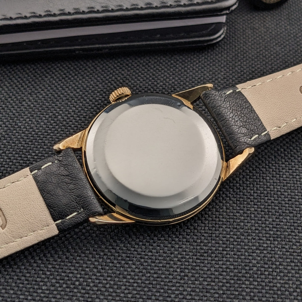 Omega Classic référence 14392-61-SC vue de l'arrière avec un fond de boîtier lisse et réfléchissant et un bracelet en cuir noir sur tissu sombre.
